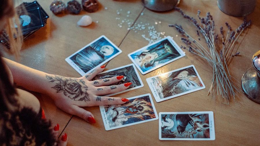 witch doing tarot card reading on table with flowers and gems